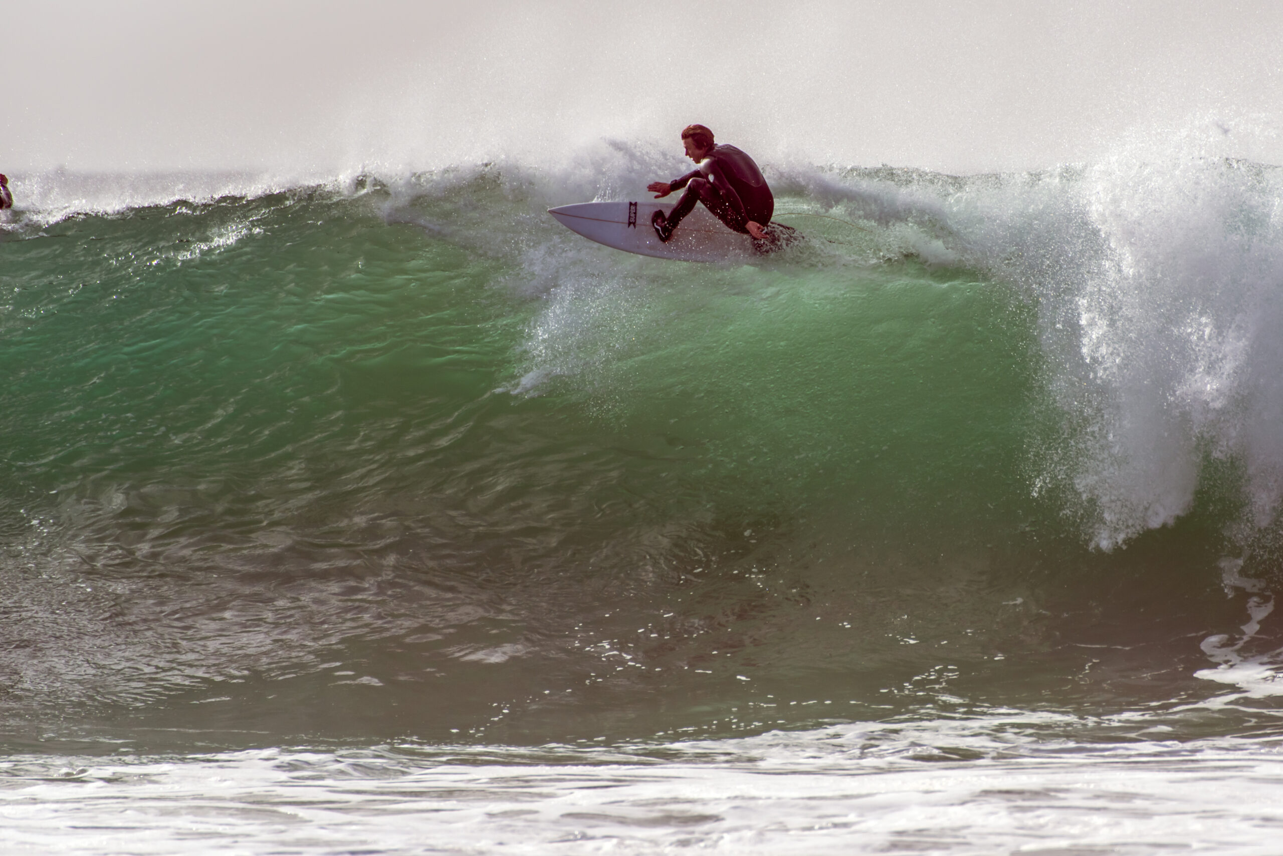 Regular foot surfer in black wetsuit flying across breaking lip while going right on large waves from winter swell in Santa Barbara, California, USA on January 9, 2019.